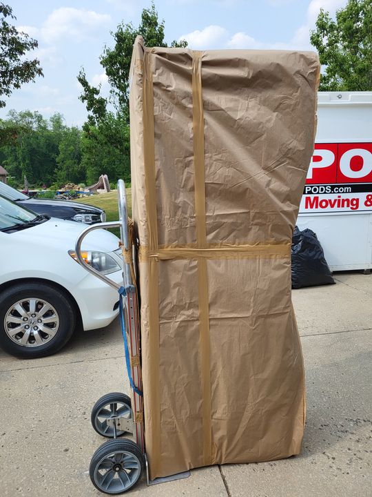 Tall paper-wrapped item on a hand truck beside a PODS container (Labor only moving) by Affordable Moving Solutions of Ohio